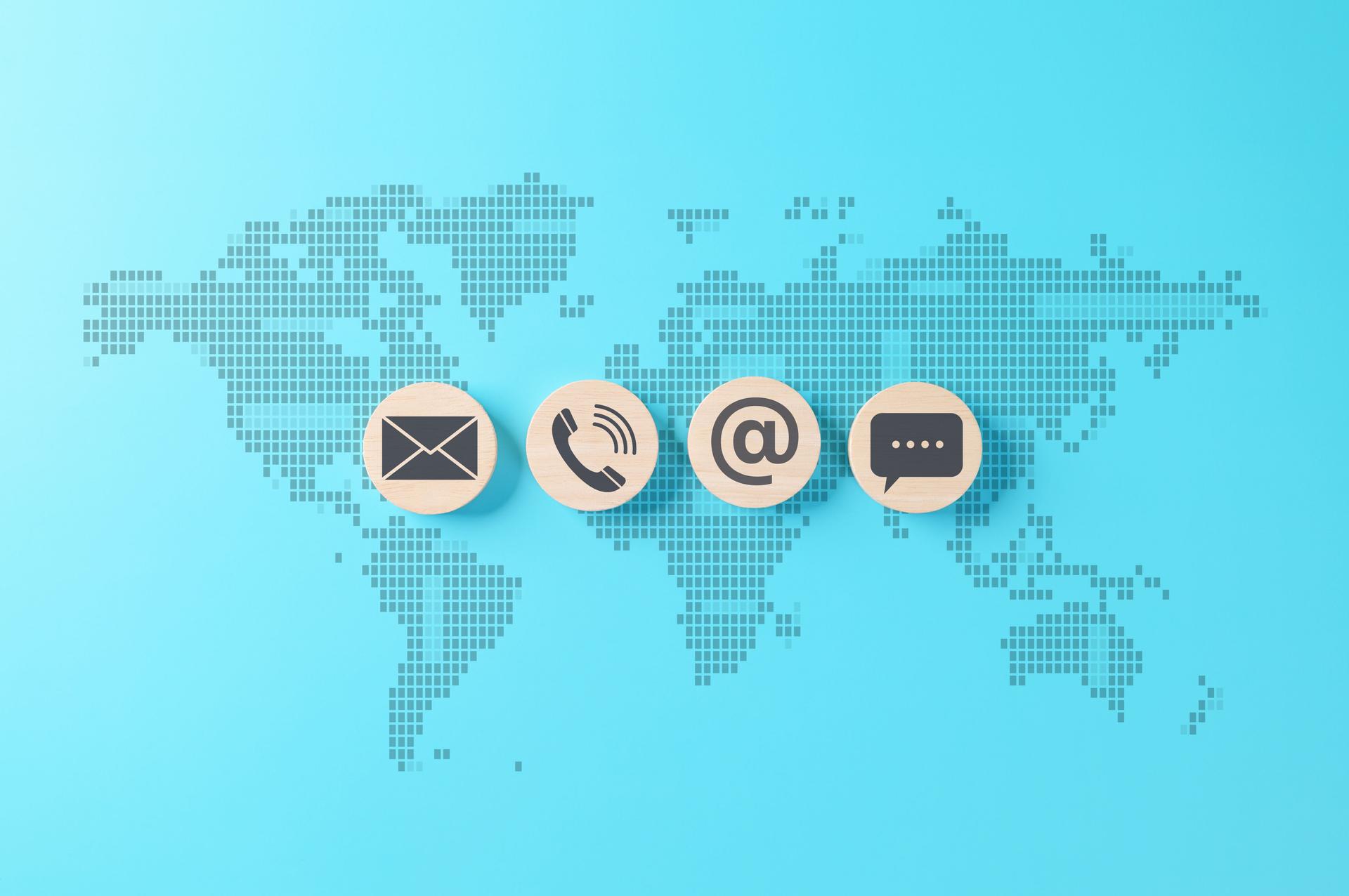 Global communication and contact us concept with email, phone, at sign, and chat icons on wooden blocks over world map background, representing customer service, technical support, business connection