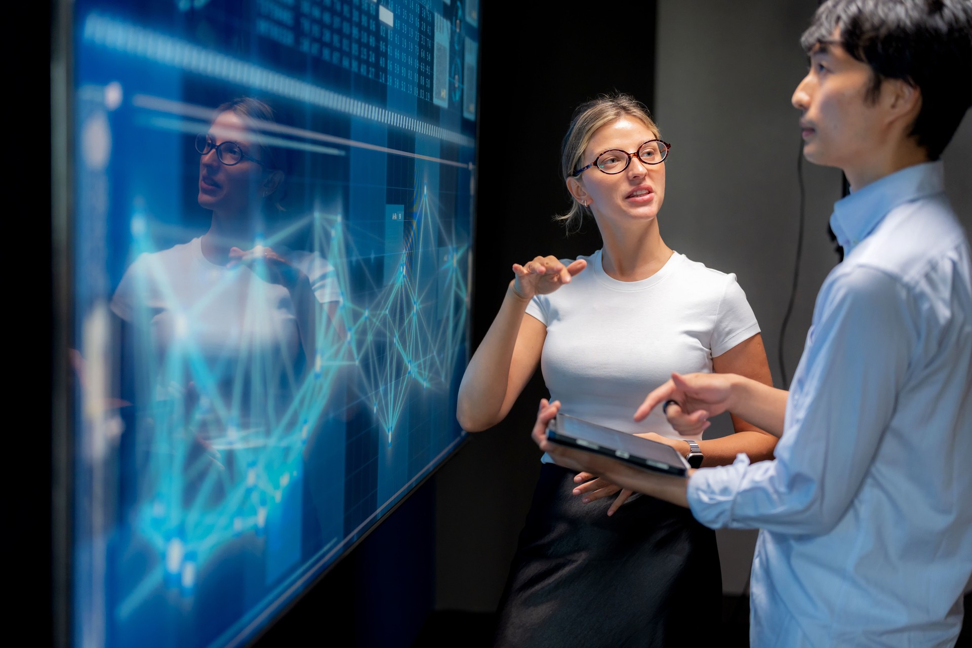 Business meeting in modern office with female programmer explaining infographic on screen to Japanese manager. Teamwork, strategy, innovation, coding, big data, AI, and technology presentation for success.